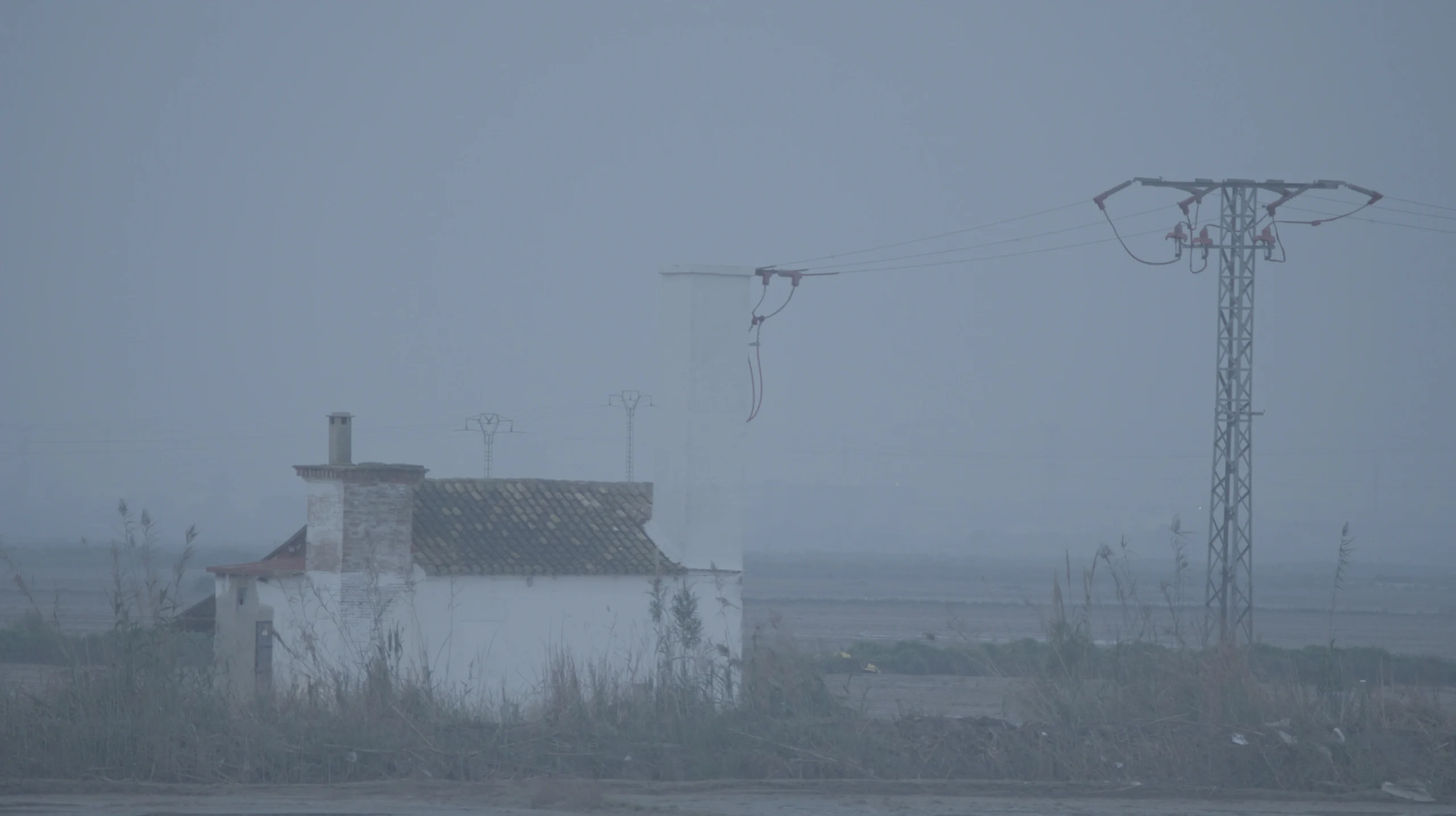 A white farmhouse and electricity pylons in thick fog — L’Aigua Recorda